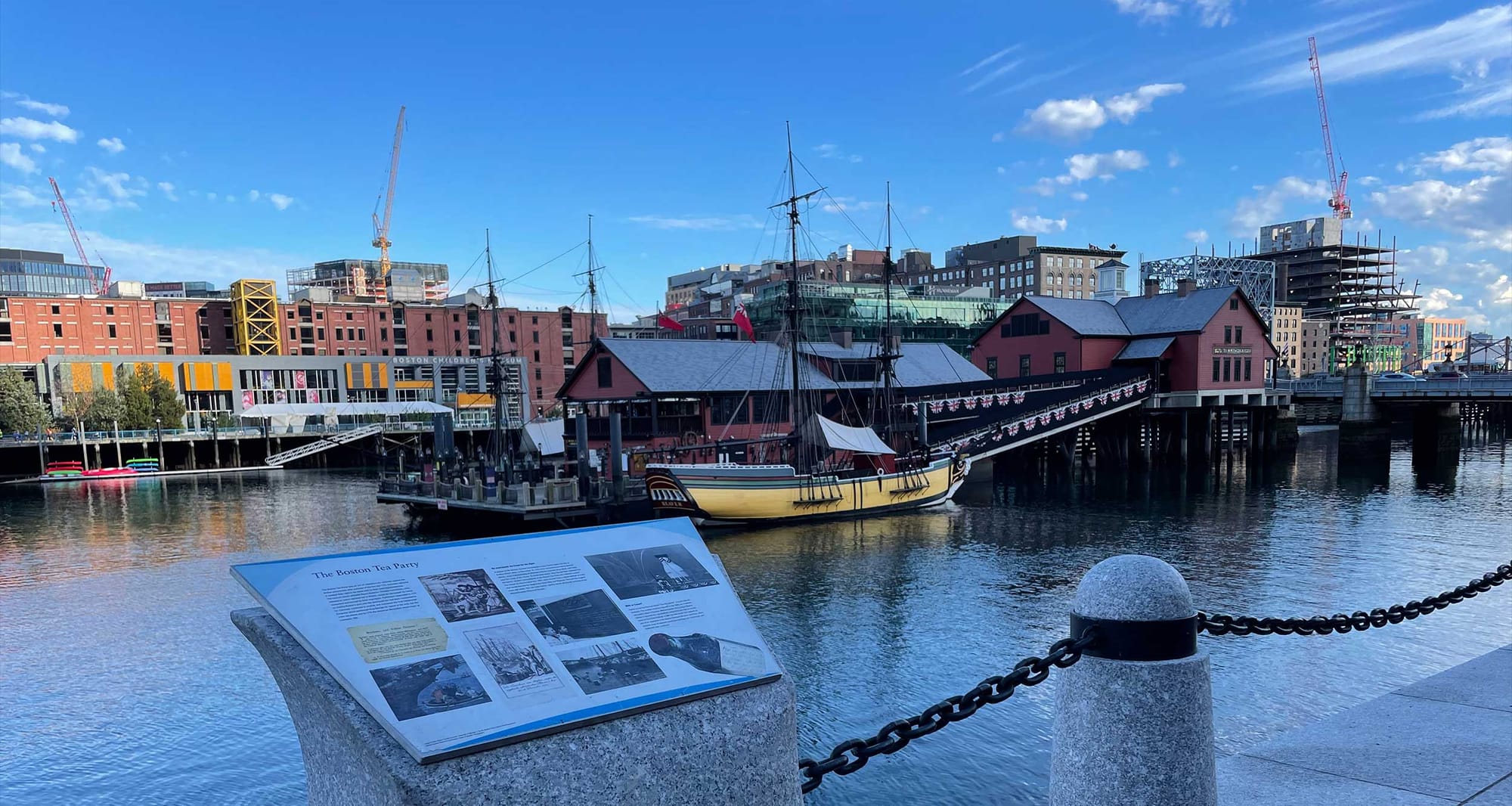 View of the children's museum and tea party museum from the harbor walk with a tourist information placard in the foreground.