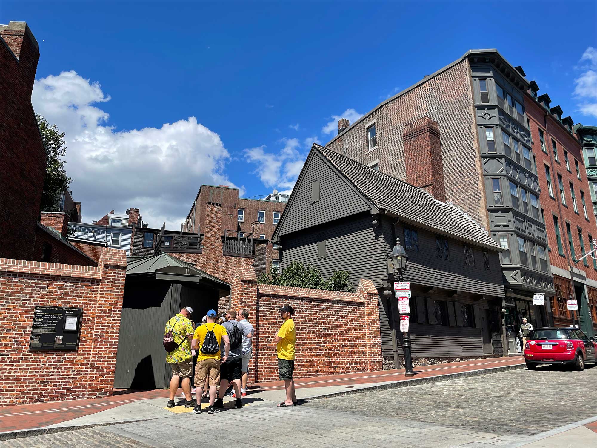 Exterior of the dark wooden three-story house with a brick wall around a courtyard.