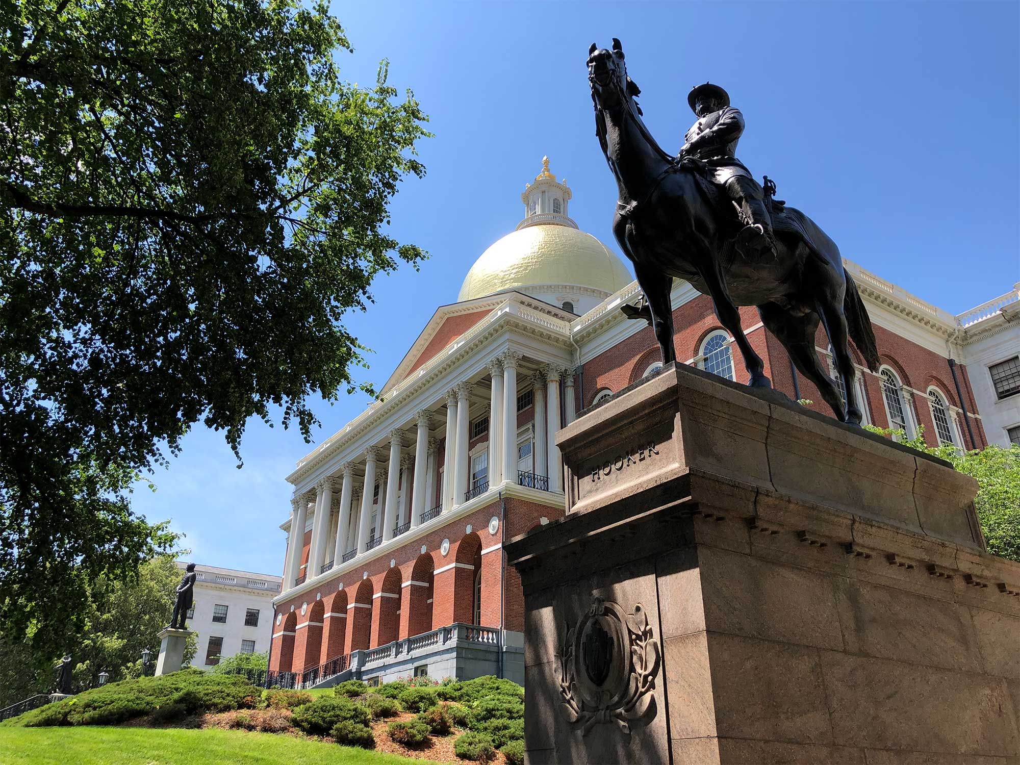 Exterior of grand state house with copper dome and a statue of a man on horseback in the foreground.