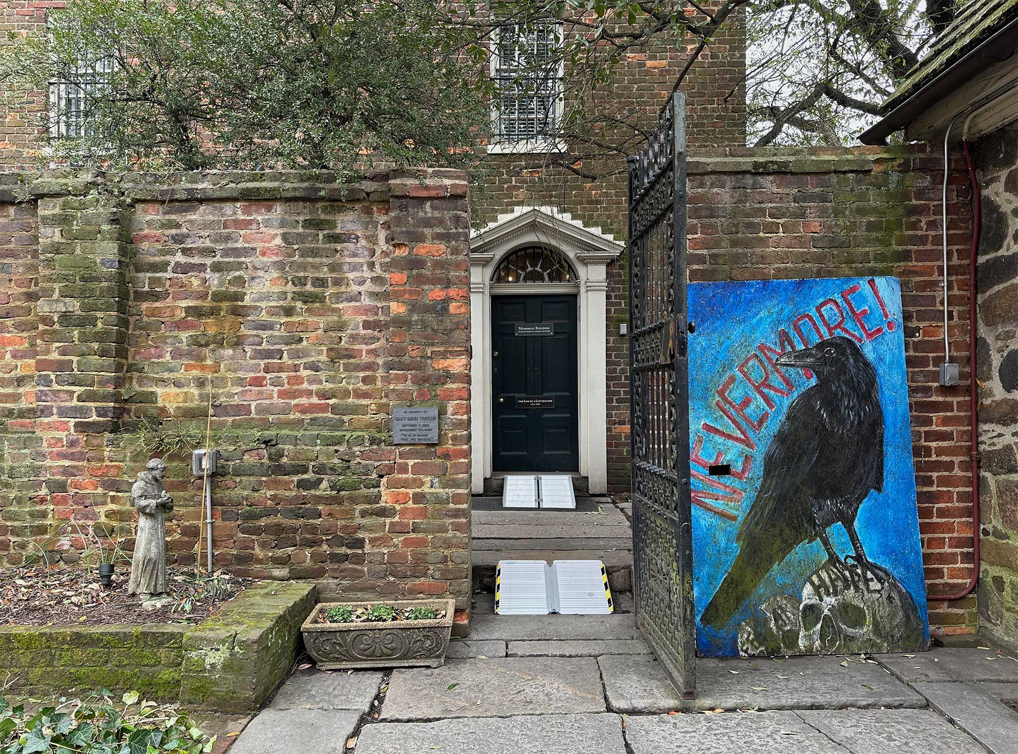 Portable wheelchair ramps providing access to old building, large painting of raven propped up outside one building.