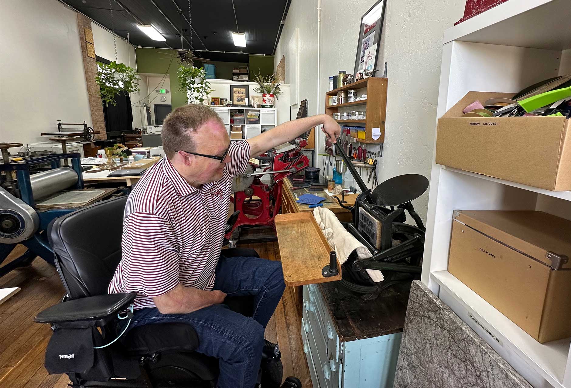 John using a historic printing press to apply a design to a canvas bag.