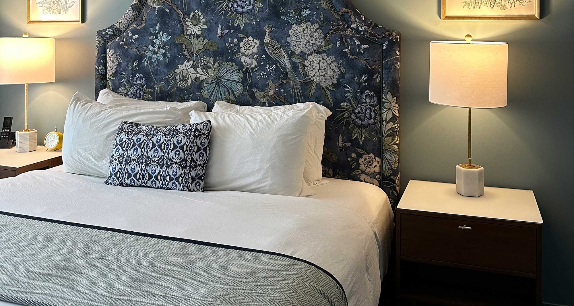 Close up of bed with floral nightstand in hotel room.