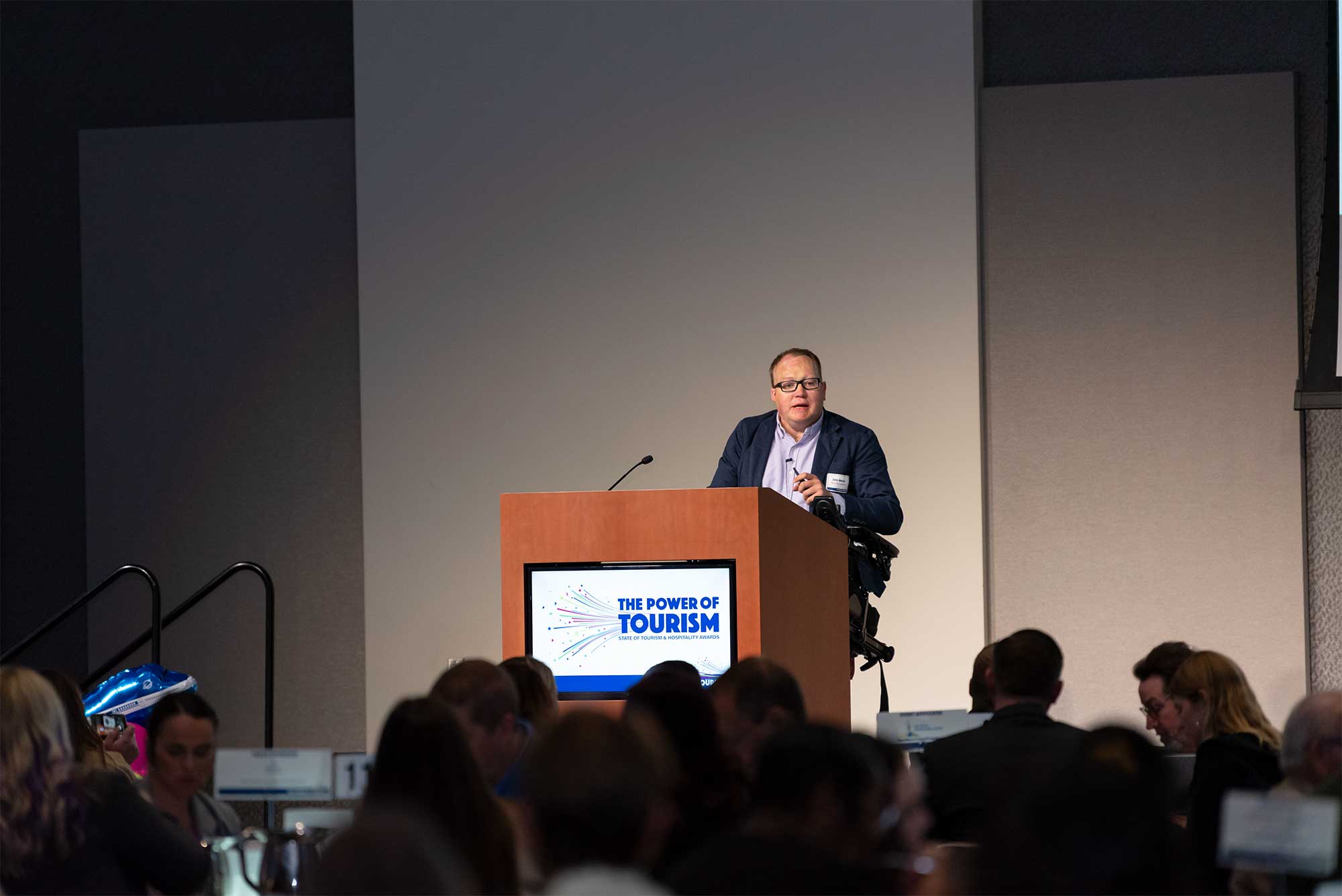 John on stage behind the podium at an event of some 300 travel professionals and business owners.